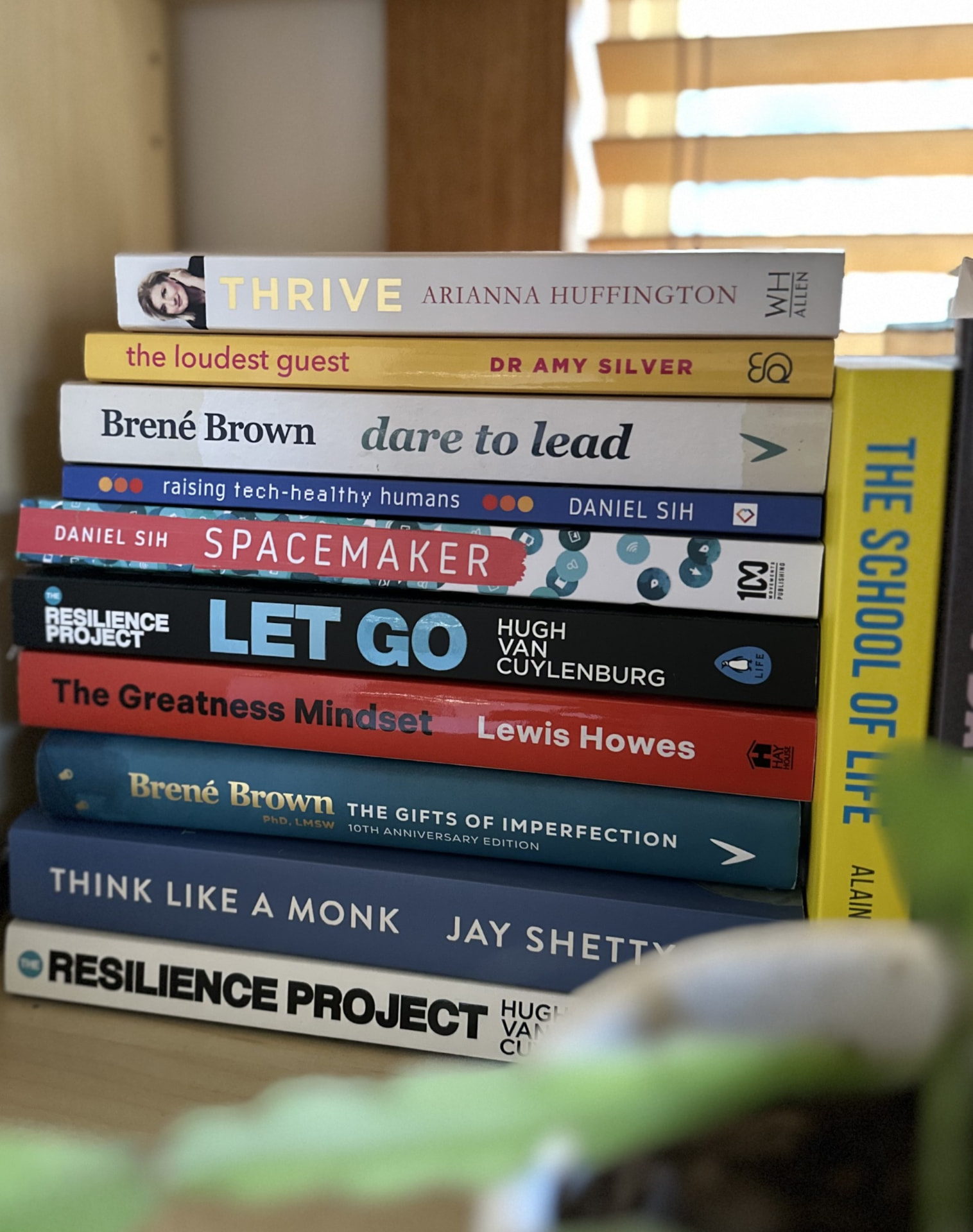 A stack of leadership and wellbeing books on a desk in soft morning light